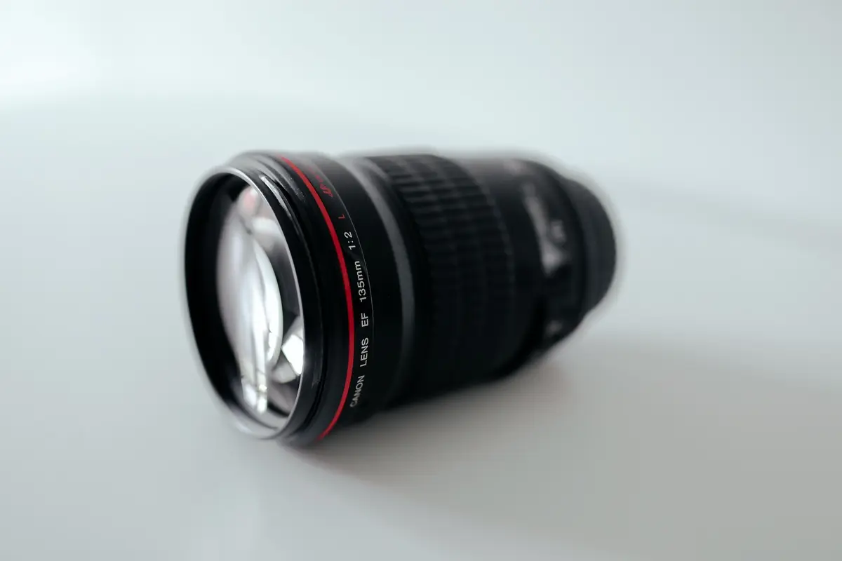 Canon EF 135mm f/2 L lens with a red ring near the front, seen at an angle against a light background